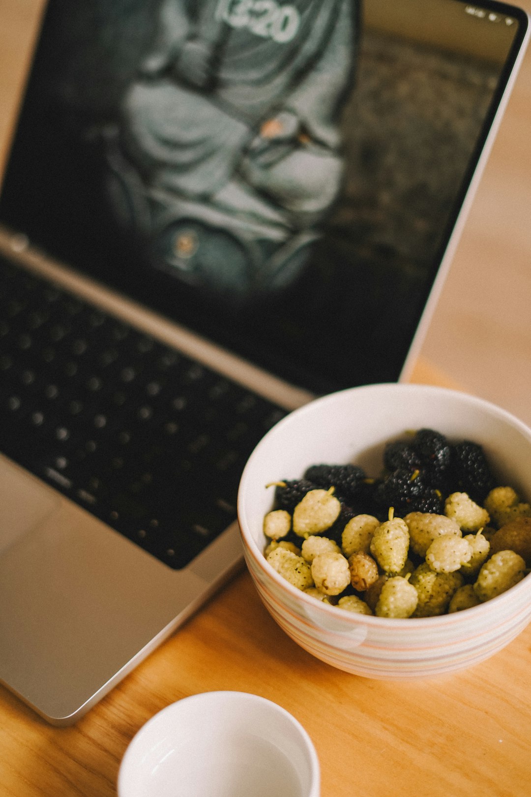 a-bowl-of-food-next-to-a-laptop-on-a-table-aebaiwtyhzw